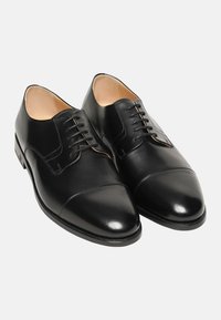 Chaussures habillées en cuir noir avec une finition lisse, bout pointu et système de laçage à six œillets. Caractérisées par des accents de couture subtils sur le dessus.