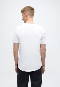 T-shirt bianca in cotone con maniche corte, orlo arrotondato e texture liscia, vista da dietro.