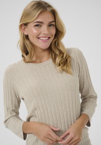 Top a coste beige con maniche a tre quarti e scollatura rotonda. Presenta una texture morbida e una silhouette aderente.