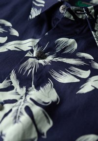 Camisa de manga corta azul marino con un gran estampado floral blanco, que presenta un detalle de botones y una suave textura de tejido.