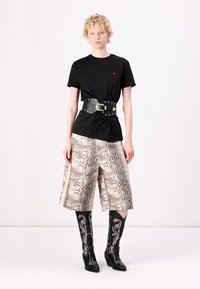 Svart t-skjorte med røde detaljer, brede shorts med slangeskrift, bred svart belte med nagler, og svarte cowboystøvler med hvite detaljer.