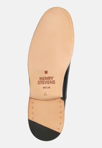 Schwarzlederne Schuhsohle mit glatter beiger Oberfläche. Verfügt über einen Markenaufdruck, Größe 4½ und dekorative Nieten an der Ferse.