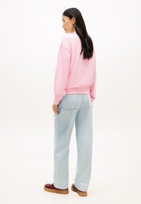 Φούτερ σε ανοιχτό ροζ χρώμα με ριμπ μανσέτες και τελείωμα, συνδυασμένο με ανοιχτό μπλε τζιν παντελόνι φαρδιάς γραμμής και μπορντό αθλητικά παπούτσια, από την πίσω όψη.