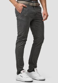 Jeans gris ajustados hechos de denim con una textura suave, que presentan bolsillos laterales y un cinturón de diseño contrastante. Llevados con zapatillas blancas.