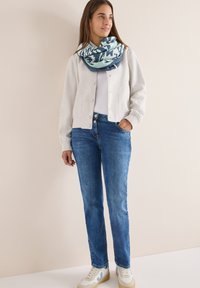 Lys grå cardigan med knapper, hvid T-shirt, blå jeans og mønstret blå tørklæde. Sneakers med hvid basis og blå detaljer.