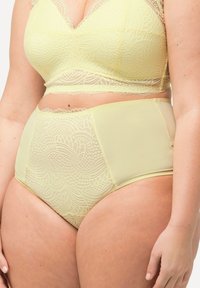 Hoog-gesneden slip in zacht geel met kantdetails, voorzien van een golvende rand en gladde mesh zijkanten voor comfort.