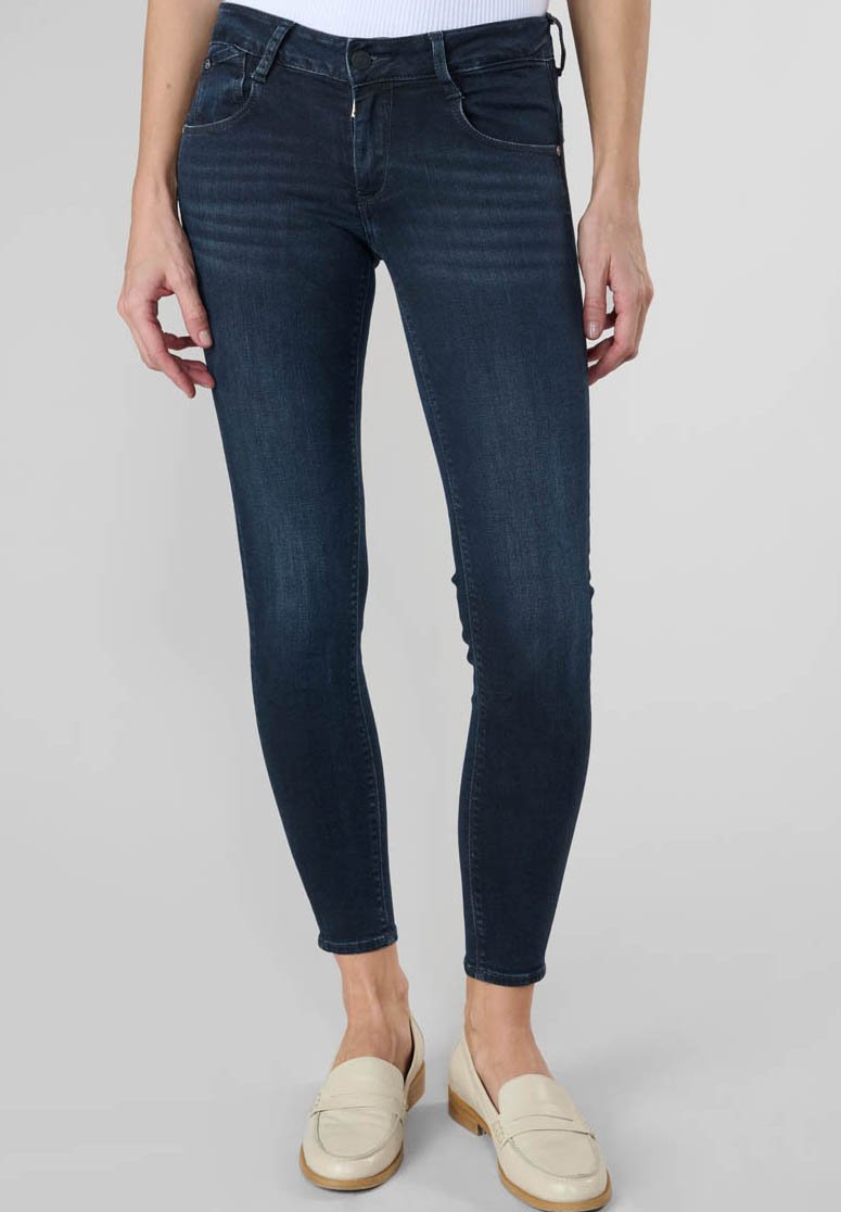 Jean skinny bleu foncé avec une taille mi-haute, en denim, avec une légère décoloration et un design classique à cinq poches, associés à des mocassins de couleur claire.