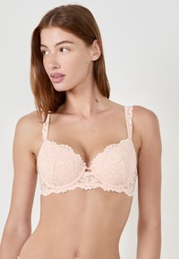 Reggiseno in pizzo rosa chiaro con motivo floreale, coppe imbottite, bordi ondulati e spalline regolabili. Presenta un dettaglio centrale a taglio.