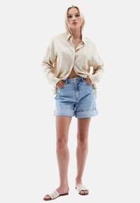 Světlé béžové košile s knoflíky, džíny šortky s ohrnutými lemy a tkané sandály na klínku. Neformální outfit, který ukazuje měkké textury a světlé barvy.