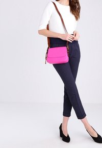 Mujer con blusa blanca y pantalones de rayas navy, llevando un bolso cruzado rosa brillante con correa marrón y tacones negros de bloque.