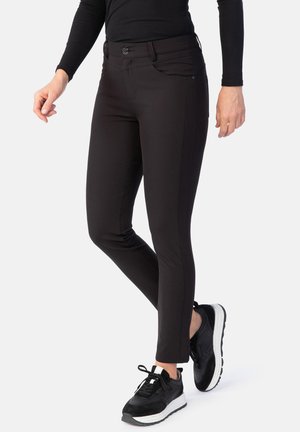 Schwarze, figurbetonte Hosen aus dehnbarem Material mit glatter Textur, vorderen Taschen und einem Knopfverschluss. Getragen mit schwarzen Sportschuhen.