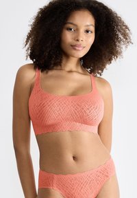Korallfärgad bralette och matchande trosor i mjukt, texturerat material, med geometriskt mönster och vågiga kanter.