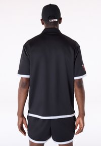 Μαύρη αθλητική φανέλα με κοντά μανίκια, με λευκή λεπτομέρεια κατά μήκος του γιακά και των άκρων των μανικιών. Συνδυάζεται με αντίστοιχο μαύρο σορτς.