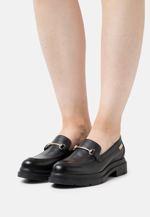 Zwarte leren instappers met een ronde neus, decoratieve gouden hardware en een gestructureerde riem. Dikke zwarte rubberen zool voor extra hoogte.