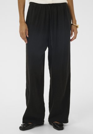 Fekete, széles szárú nadrág texturált anyagból, gumis derékpánttal és állítható húzózsinórral, fekete lapos cipővel párosítva.