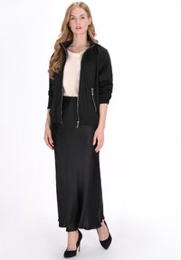 Fekete bomber dzseki ezüst cipzárokkal, krémszínű felső és fekete szatén szoknya fölött viselve, testhez simuló szabással és magassarkú cipőkkel.