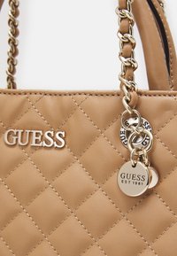 Brun quiltet håndtaske med guldfarvet hardware, der har et logo og charms detalje. Materialet ser glat ud med synlig syning.