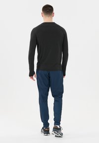 Schwarzes Longsleeve-Shirt mit Rundhals, kombiniert mit dunkelblauen Sporthosen. Das Outfit umfasst schwarze Laufschuhe mit strukturierten Oberflächen.