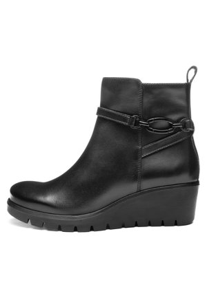 Black leather ankle boot with wedge sole, decorative strap, and metal chain detail, featuring a pull tab at the back.