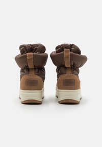 Botines tobilleros marrones tipo puffer con un acento de ante, con cuello acolchado, lengüeta para tirar y suela blanca resistente. Vista trasera que muestra los detalles del diseño.