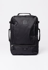 Black backpack made of durable fabric, featuring a top handle, adjustable straps, and a front zip pocket with a logo tag.