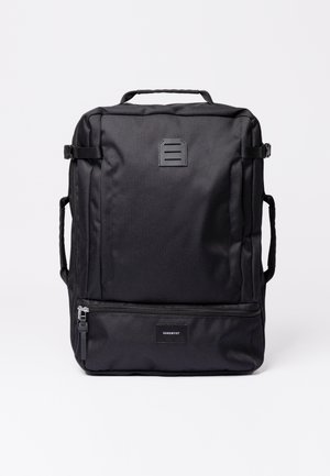 Mochila negra hecha de tejido resistente, con un asa superior, correas ajustables y un bolsillo delantero con cremallera que lleva una etiqueta de logo.