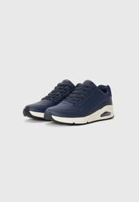 Navy blue sneakers with a smooth synthetic upper, perforated detailing, cream midsole, and black textured rubber outsole. Features lace-up design.