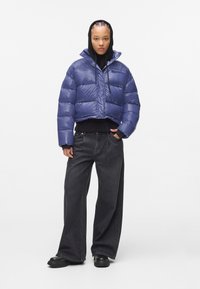 Puffy cropped jack in glanzend donkerblauw, met een hoge kraag en een trekkoord, gedragen over een zwarte trui en gecombineerd met wijde zwarte jeans.