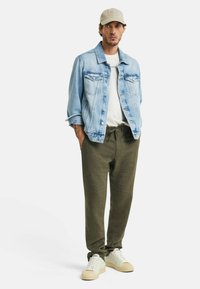 Leren spijkerjack in lichtblauw, wit T-shirt eronder, olijfgroene broek, beige sneakers met lichte accenten, casual fit, zachte texturen.