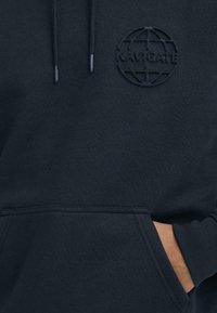 Felpa blu navy realizzata in tessuto morbido, caratterizzata da un design testurizzato del globo e la parola "NAVIGATE" impressa sul petto. Tasca frontale a canguro.