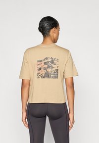 Camiseta cropped beige de mangas cortas con un gráfico de montaña en negro y rojo en la parte de atrás, hecha de suave material de algodón.
