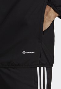 Černá sportovní bunda s logem AEROREADY, bočními kapsami a bílými třemi pruhy na rukávech. Hladká textura.