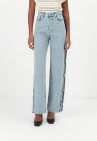 Augstās vidukļa gaišā zila džinsa bikses ar plašu piegriezumu, tām ir sānu pogu detaļas un mīksta tekstūra. Izstrādātas komfortam.