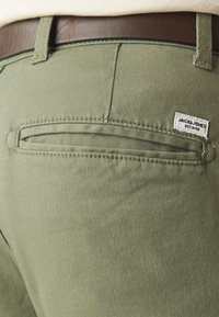 Pantalones verde oliva con una tela texturizada, que cuentan con un bolsillo trasero de abertura estrecha y una etiqueta de marca cosida en él.