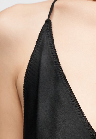 Κοντινή λήψη σε μαύρο ρούχο με λεπτές τιράντες και διακοσμητική ραφή στην άκρη, που φοριέται σε γυμνό δέρμα στον ώμο και το στήθος.