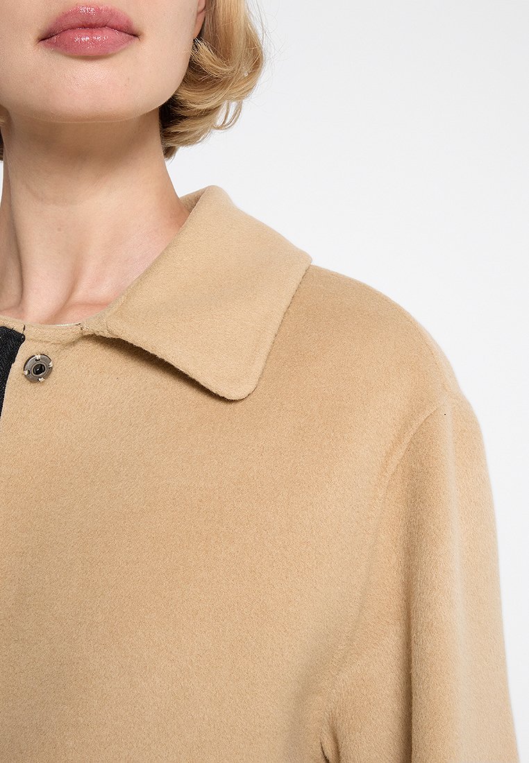 Abrigo de lana beige con un amplio collar y detalles de botones negros, que presenta una textura suave y una silueta estructurada.