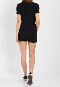 Haut noir à manches courtes associé à un short noir, offrant une coupe décontractée et une taille élastique. Des baskets avec des accents blancs et noirs sont portées.