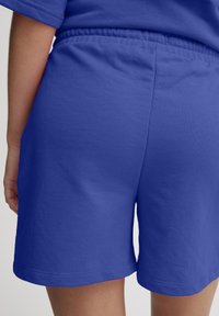 Shorts en coton bleu avec une taille élastique, dotés d'une texture lisse et d'un ourlet, présentés de dos avec une coupe décontractée.