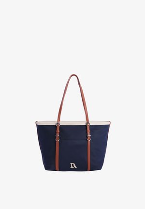 Bolsa tote azul marino con ribete crema y correas de hombro ajustables marrones, con el logo plateado DA en el bolsillo delantero.