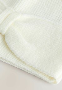 Cream-colored knit fabric with a textured surface. Features a folded design and bow detail, showcasing a soft and cozy appearance.