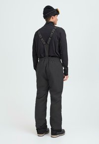 Black insulated snow pants with adjustable straps, elastic waistband, and reinforced cuffs, worn over a long-sleeve black top.