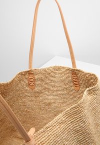 Borsa a rete in paglia intrecciata con manici in pelle marrone chiaro e cuciture a contrasto. Bordo superiore arrotondato con dettagli intrecciati sulle attacchi dei manici.