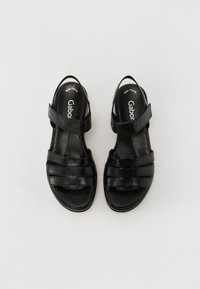 Sandales en cuir noir avec bout et talon ouverts, présentant plusieurs brides à l'avant et une bride de cheville ajustable. Texture lisse, design minimaliste.