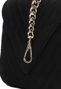 Zwarte suède tas met een gequilte ontwerp, gouden kettingriem en een sluiting voor veilige sluiting. Gladde textuur met een glanzende metalen afwerking.