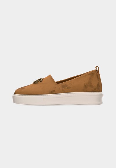Καφέ σουέτ παπούτσι τύπου slip-on με λευκή παχιά σόλα και διακοσμητική μεταλλική λεπτομέρεια στο πάνω μέρος, σε πλάγια όψη πάνω σε απλό φόντο.