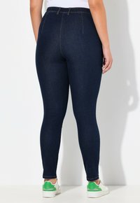 Leggings de denim azul oscuro con cintura alta y corte ajustado. La tela tiene una textura suave, con bolsillos traseros y costuras sutiles.