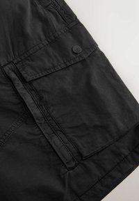 Tissu noir avec une grande poche rectangulaire dotée d'un rabat et d'une fermeture par bouton noir rond sur le côté supérieur droit.