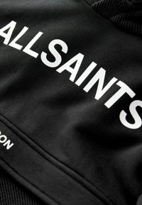 Tela negra con el texto blanco "ALLSAINTS" impreso en letras mayúsculas y en negrita.