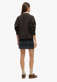 Ciemnobrązowa, oversize'owa bluza z opuszczonymi ramionami, zestawiona z krótką granatową kratkowaną spódnicą i masywnymi brązowymi butami. Widoczne są dziergane skarpety.