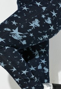 Blauwe denim jeans met een sterrenpatroon in lichtblauw, met een vervaagde textuur. Close-up van de stof en ontwerpdDetails.